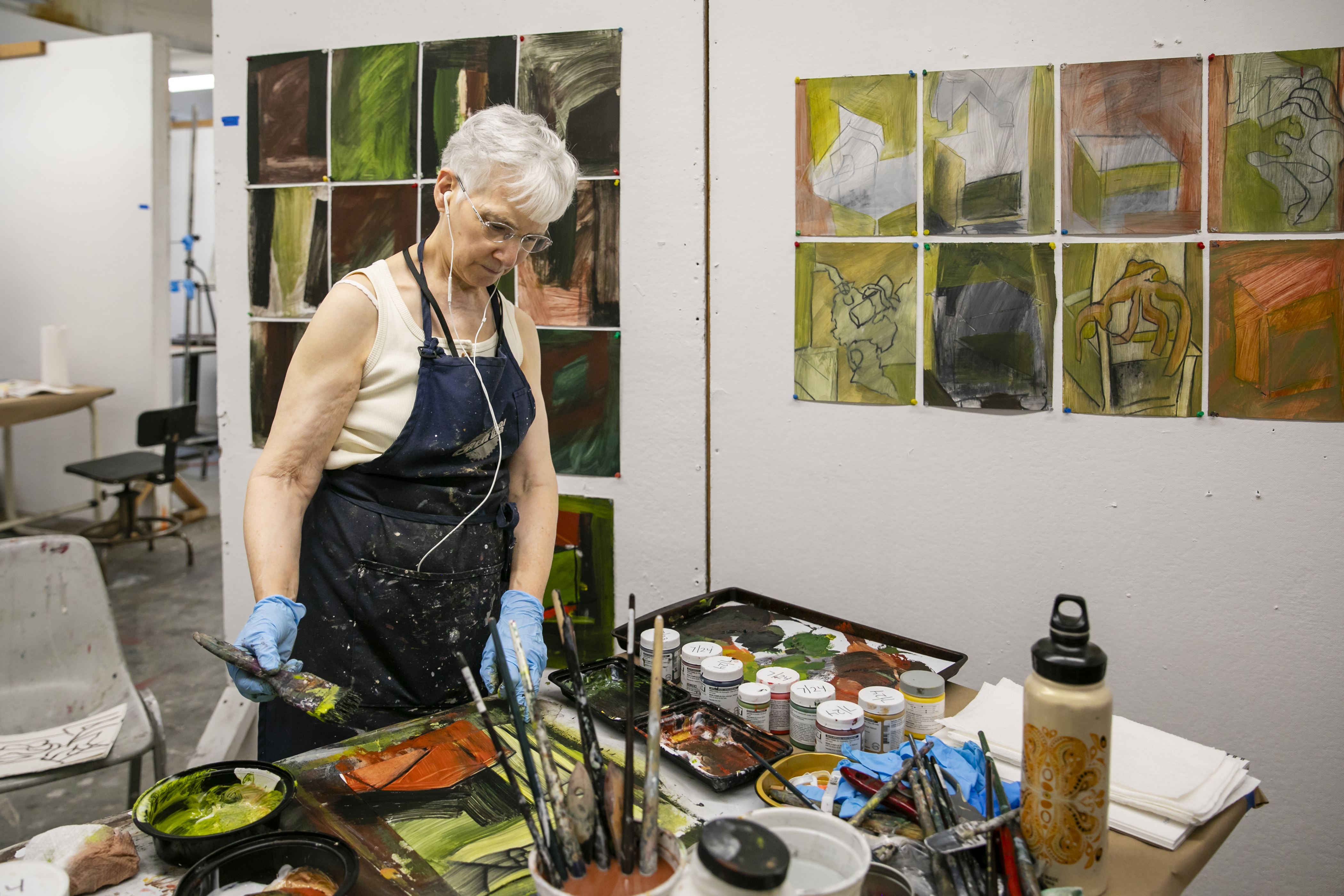 Women in art studio, paintings on wall, mixing paint at a table